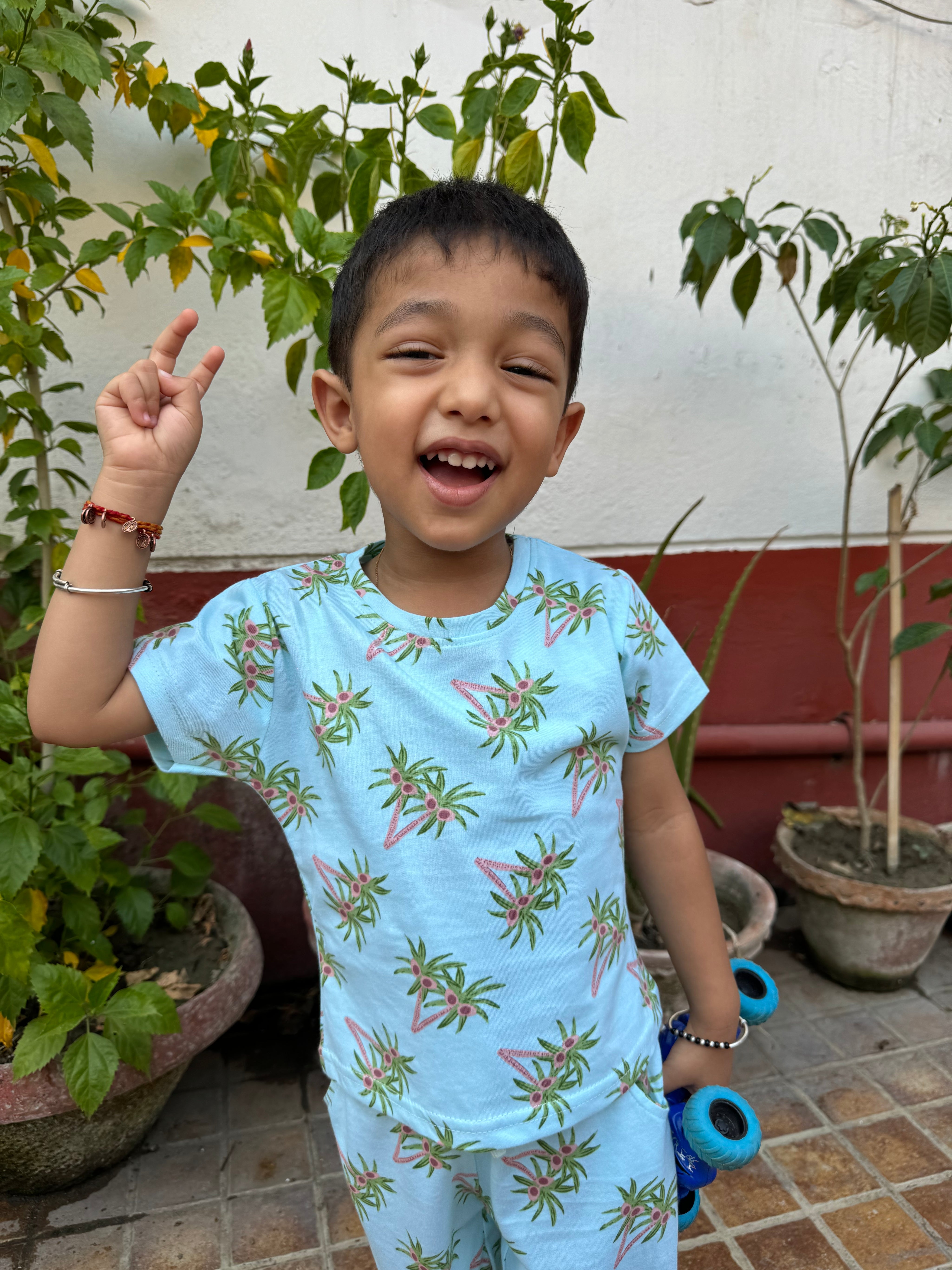 A child wearing unisex topical print nightwear for kids, holding a toy and showing a V sign