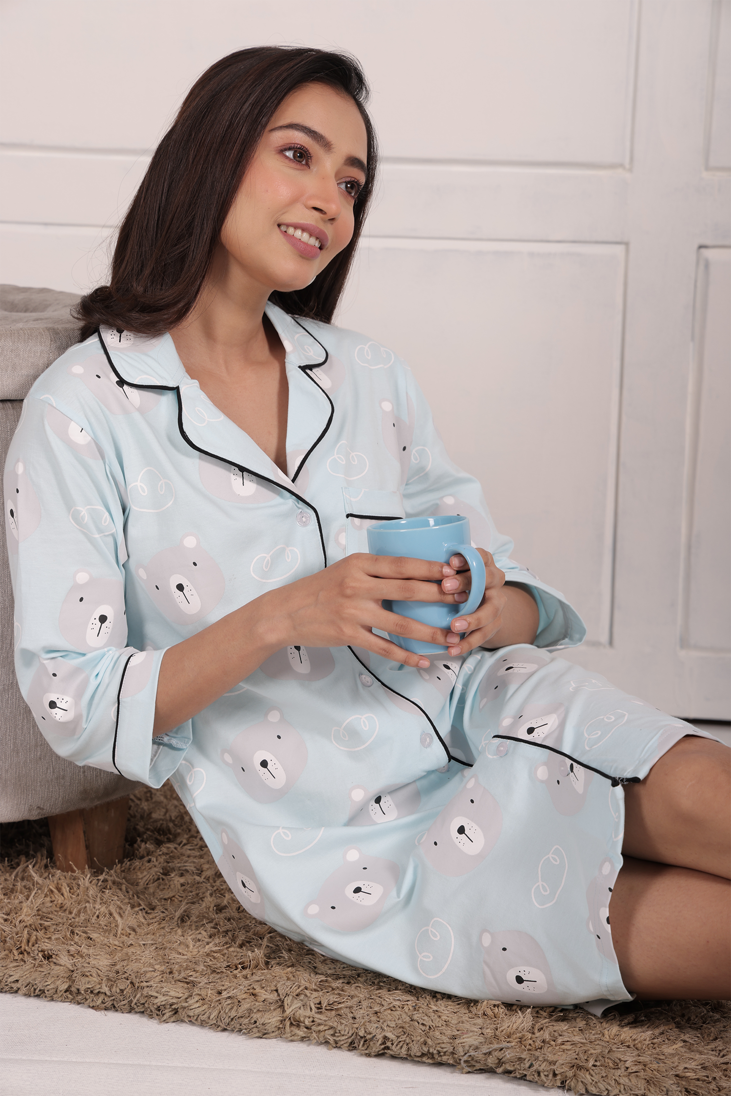 A girl reclining, holding a cup with both hands, wearing a Teddy Print Sleep Shirt nightwear by NapStory