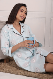 A girl reclining, holding a cup with both hands, wearing a Teddy Print Sleep Shirt nightwear by NapStory