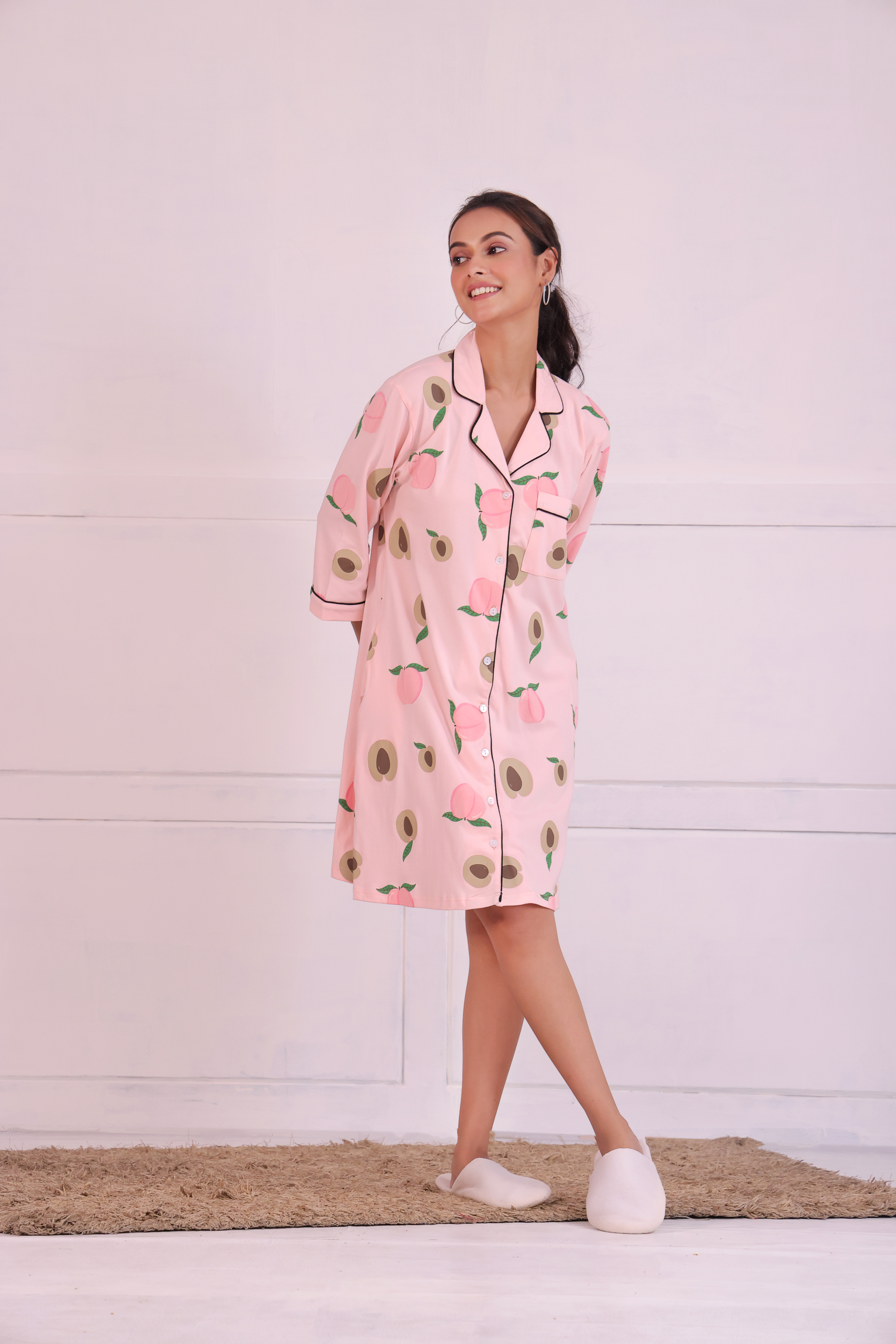 Young girl in a Pink Colour Peach Print Sleep Shirt nightwear by NapStory, standing cheerfully with legs crossed.