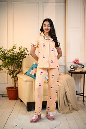 Woman standing in a peach Love Bulb Print Pyjama Set by NapStory, styled with playful bulb patterns, perfect for nightwear or lounging.