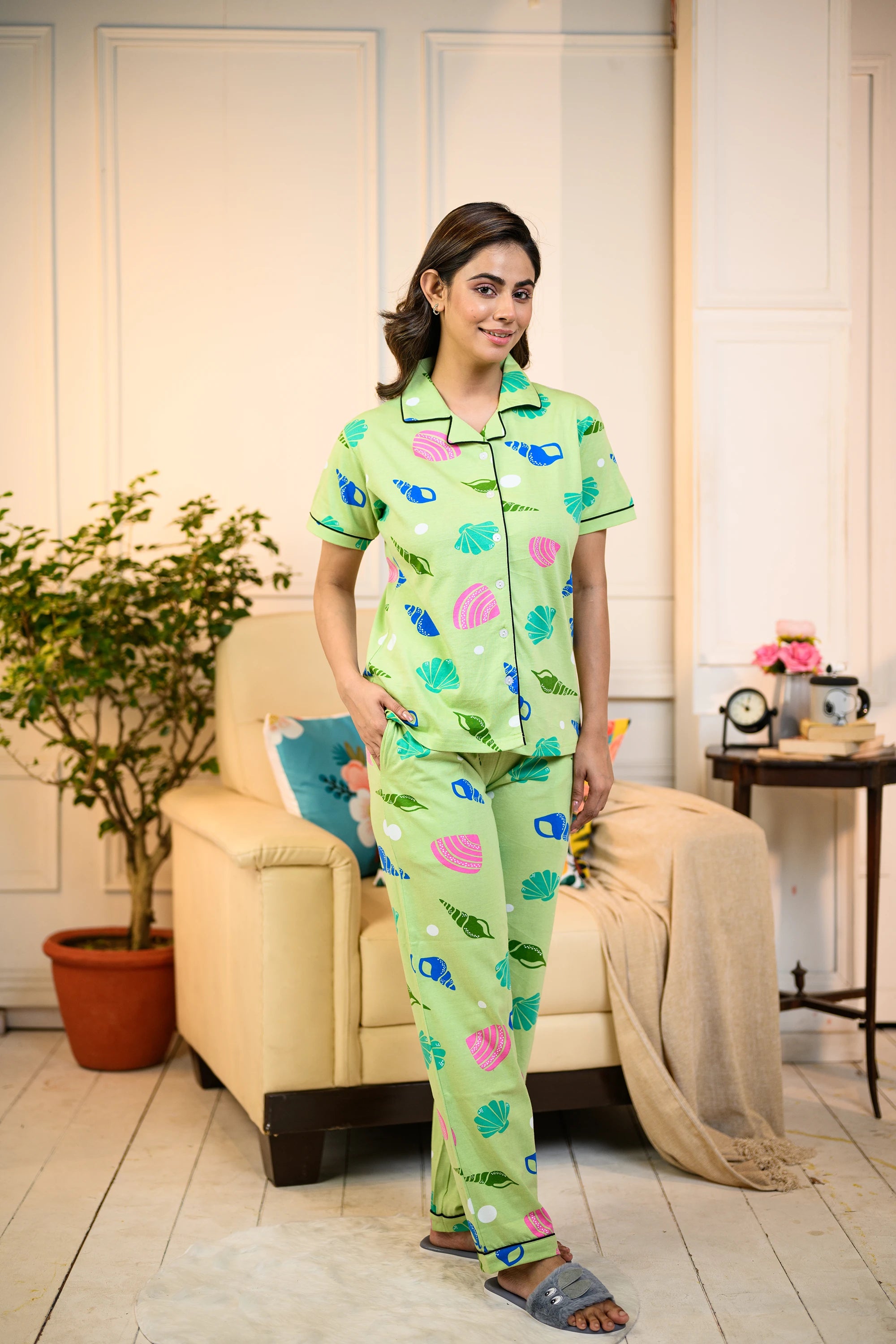 Woman wearing a green Sea Shell Print Pyjama Set by NapStory, standing in a cozy living room with casual home decor.