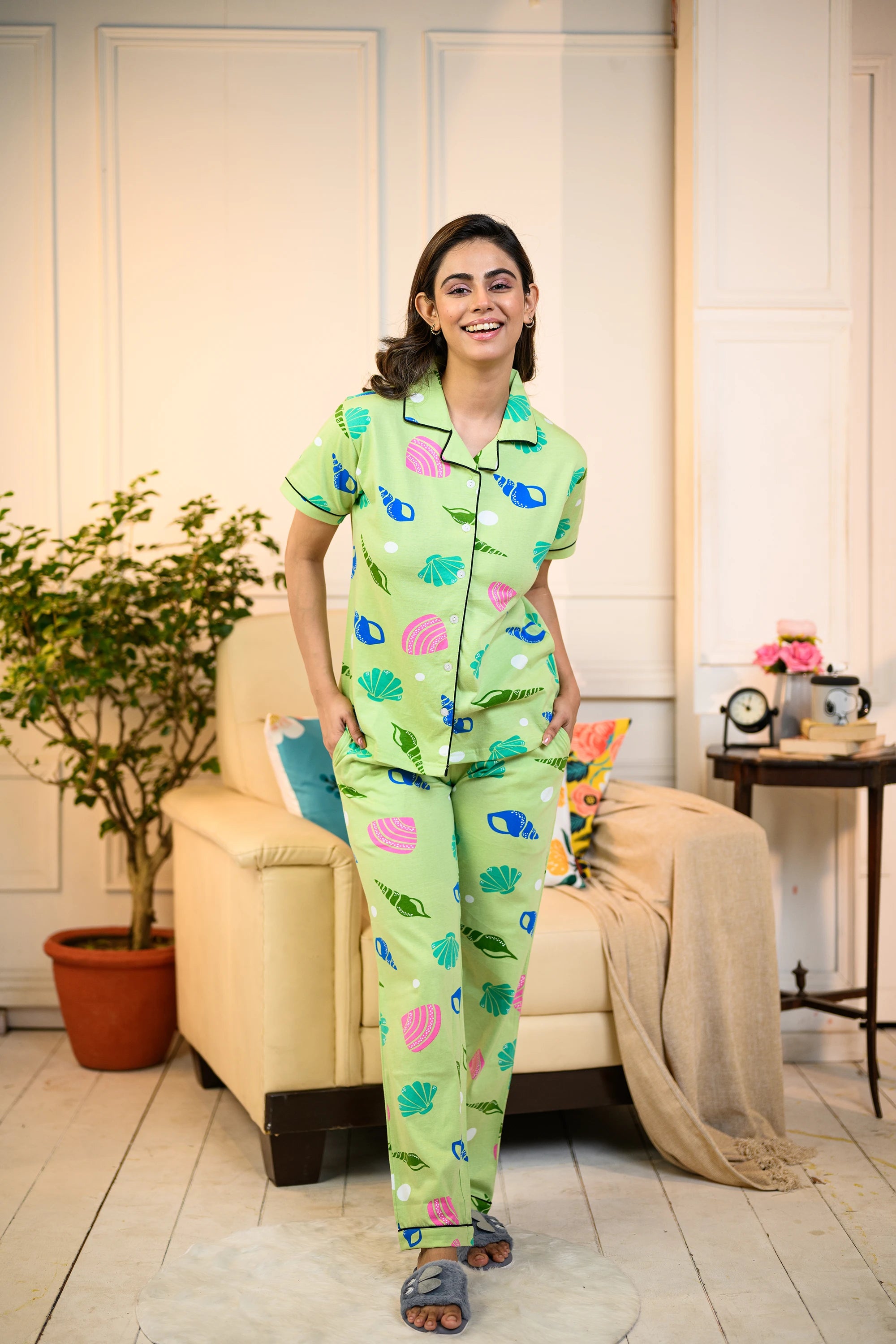 Woman smiling while wearing a green Sea Shell Print Pyjama Set by NapStory, featuring colorful shell patterns, styled for nightwear or loungewear.