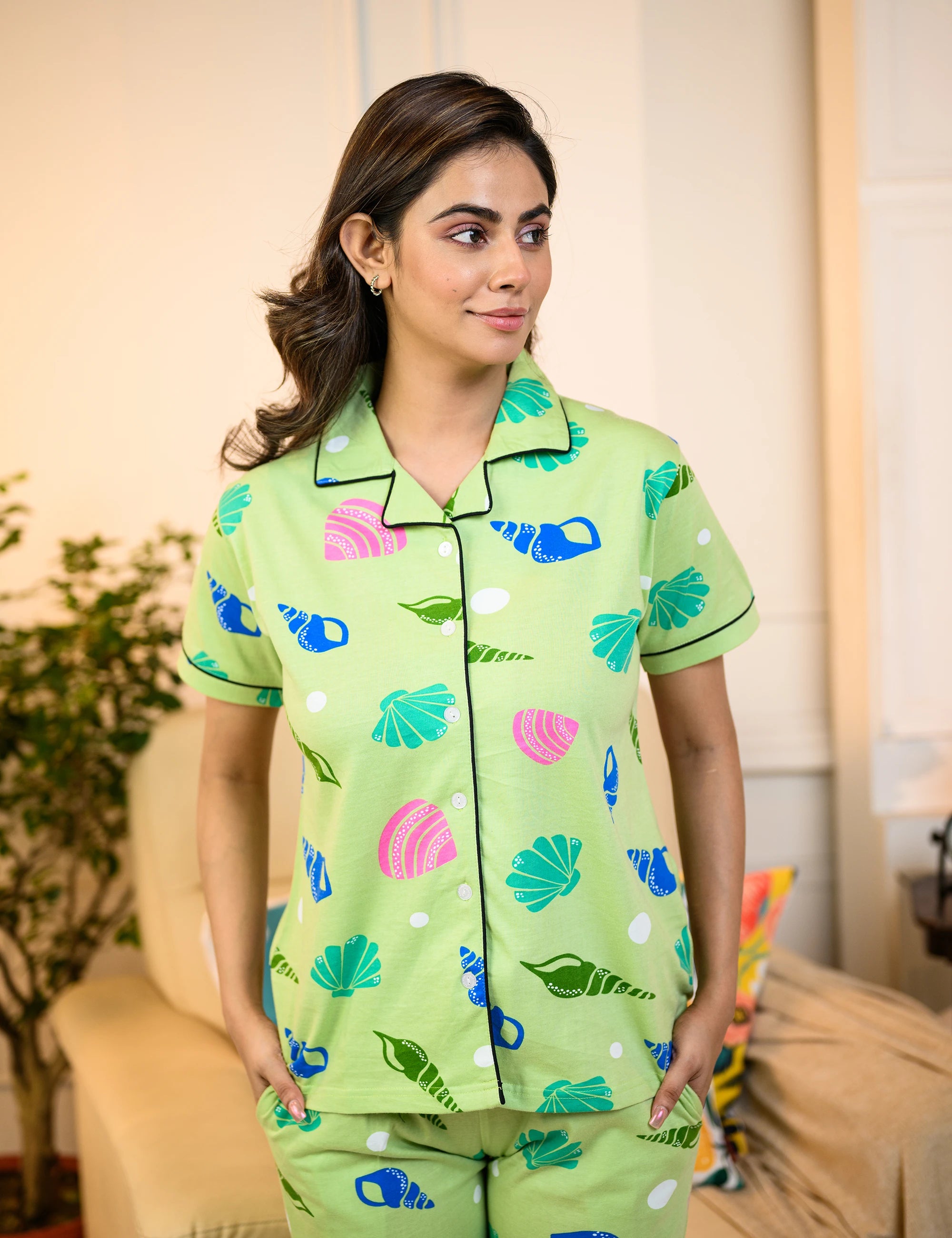 Woman wearing a vibrant green Sea Shell Print Pyjama Set by NapStory, featuring colorful shell designs, crafted from breathable 100% cotton fabric for ultimate comfort.