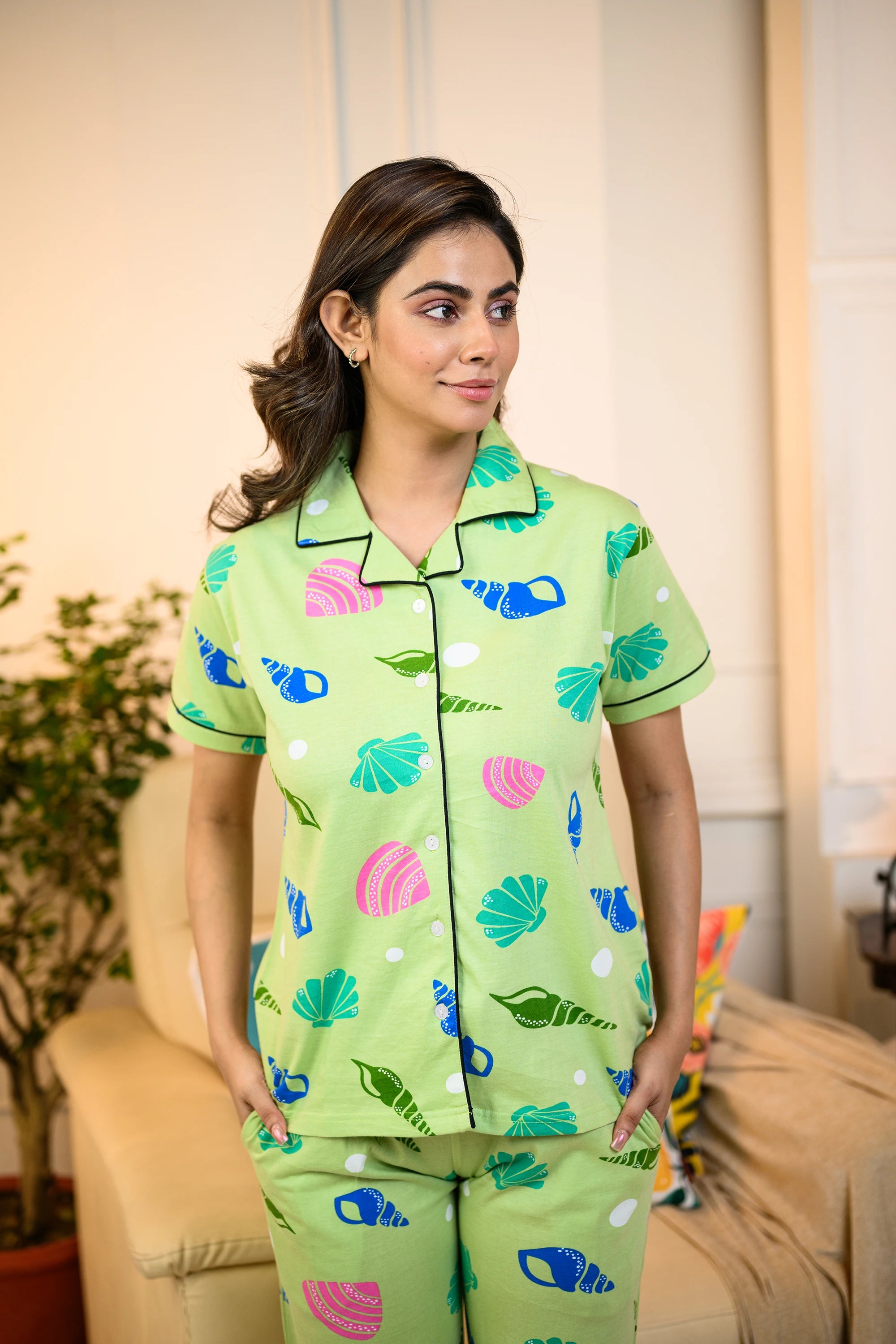 Woman wearing a vibrant green Sea Shell Print Pyjama Set by NapStory, featuring colorful shell designs, crafted from breathable 100% cotton fabric for ultimate comfort.