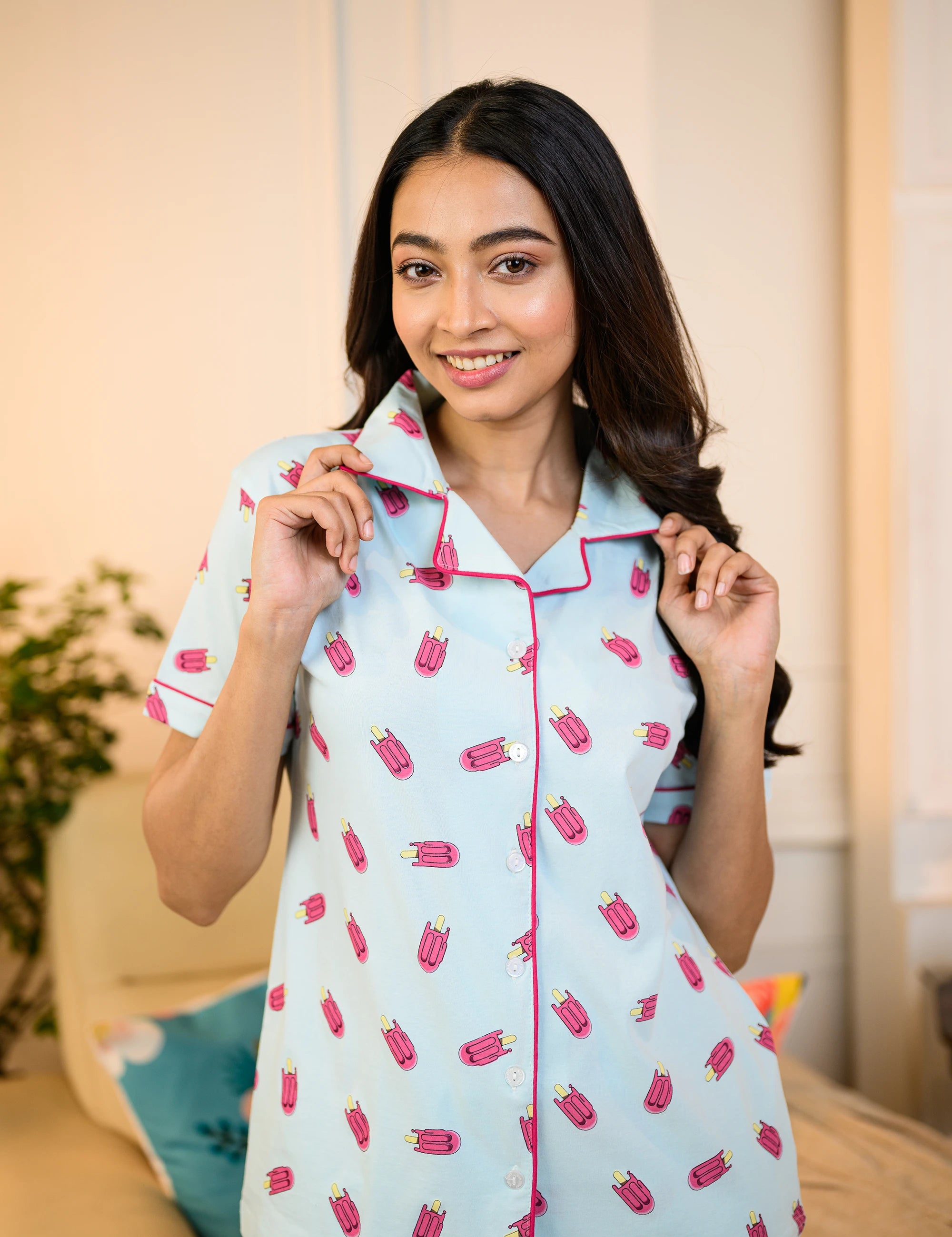 A woman smiles while adjusting her collar, wearing the Popsicle Print Pyjama Set by NapStory, highlighting the playful design.