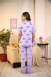 Back view of a purple panda print pyjama set featuring adorable panda motifs and relaxed fit, worn by a woman standing in a cozy living room