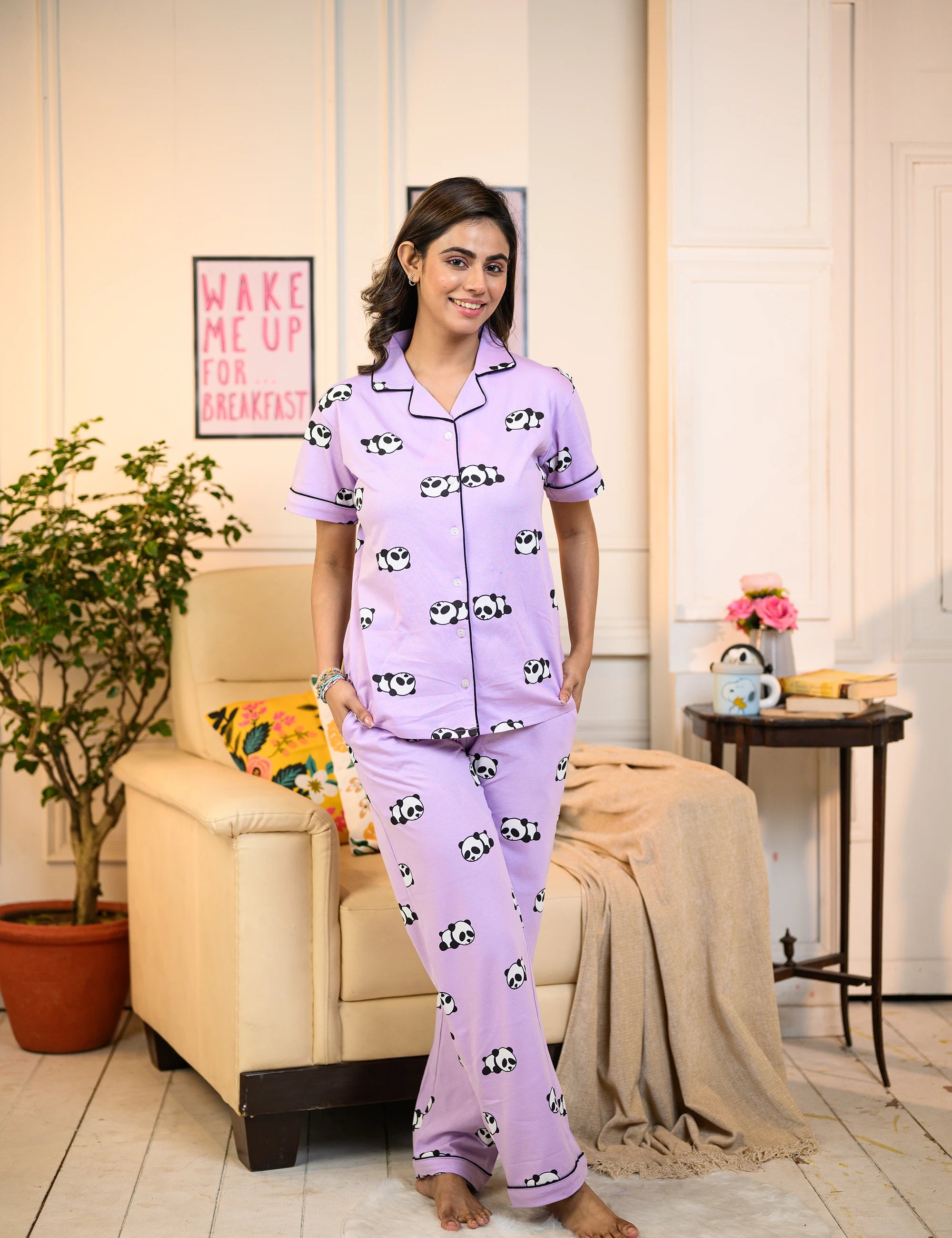 A woman wearing a purple panda print pyjama set, standing in a cozy room