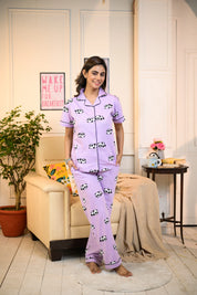 A woman wearing a purple panda print pyjama set, standing in a cozy room