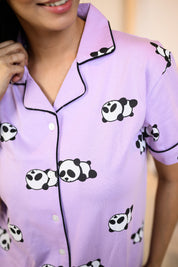 Close-up of a purple panda print pyjama top showcasing detailed black piping on the collar and playful panda designs, with a partial view of the wearer smiling.