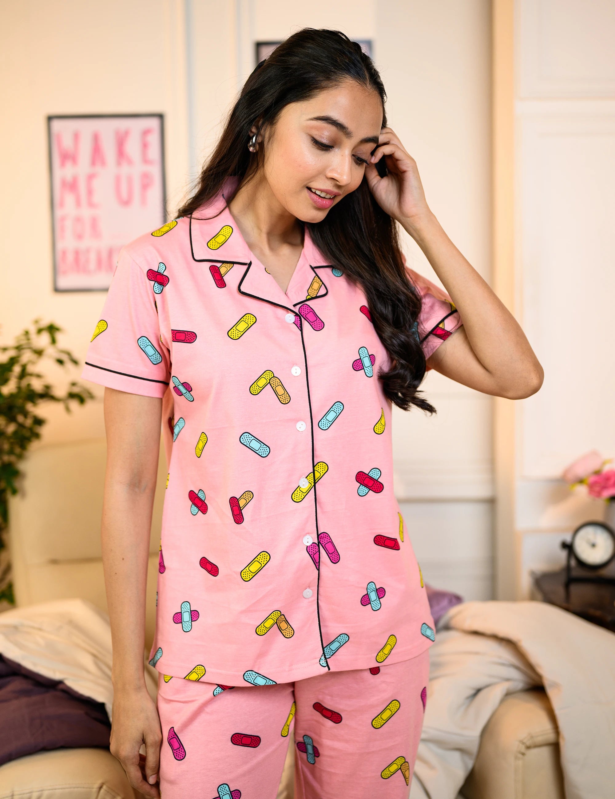 Woman wearing a pink Bandage Print Pyjama Set with colorful bandage patterns, standing in a cozy living room.