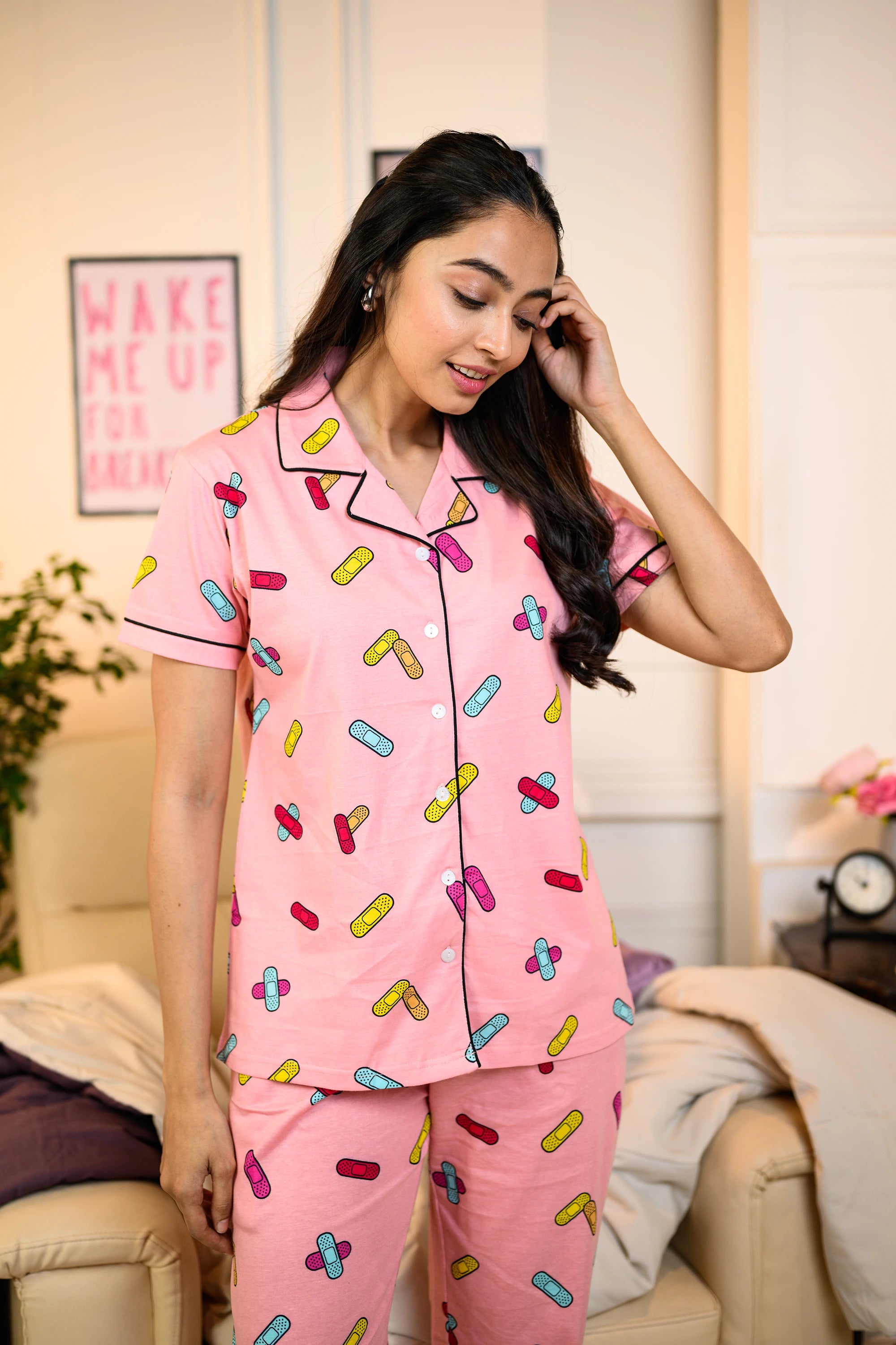 Woman wearing a pink Bandage Print Pyjama Set with colorful bandage patterns, standing in a cozy living room.