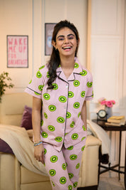 Woman wearing a pink Kiwi Print Pyjama Set by NapStory, featuring vibrant green kiwi patterns, styled for cozy nightwear.