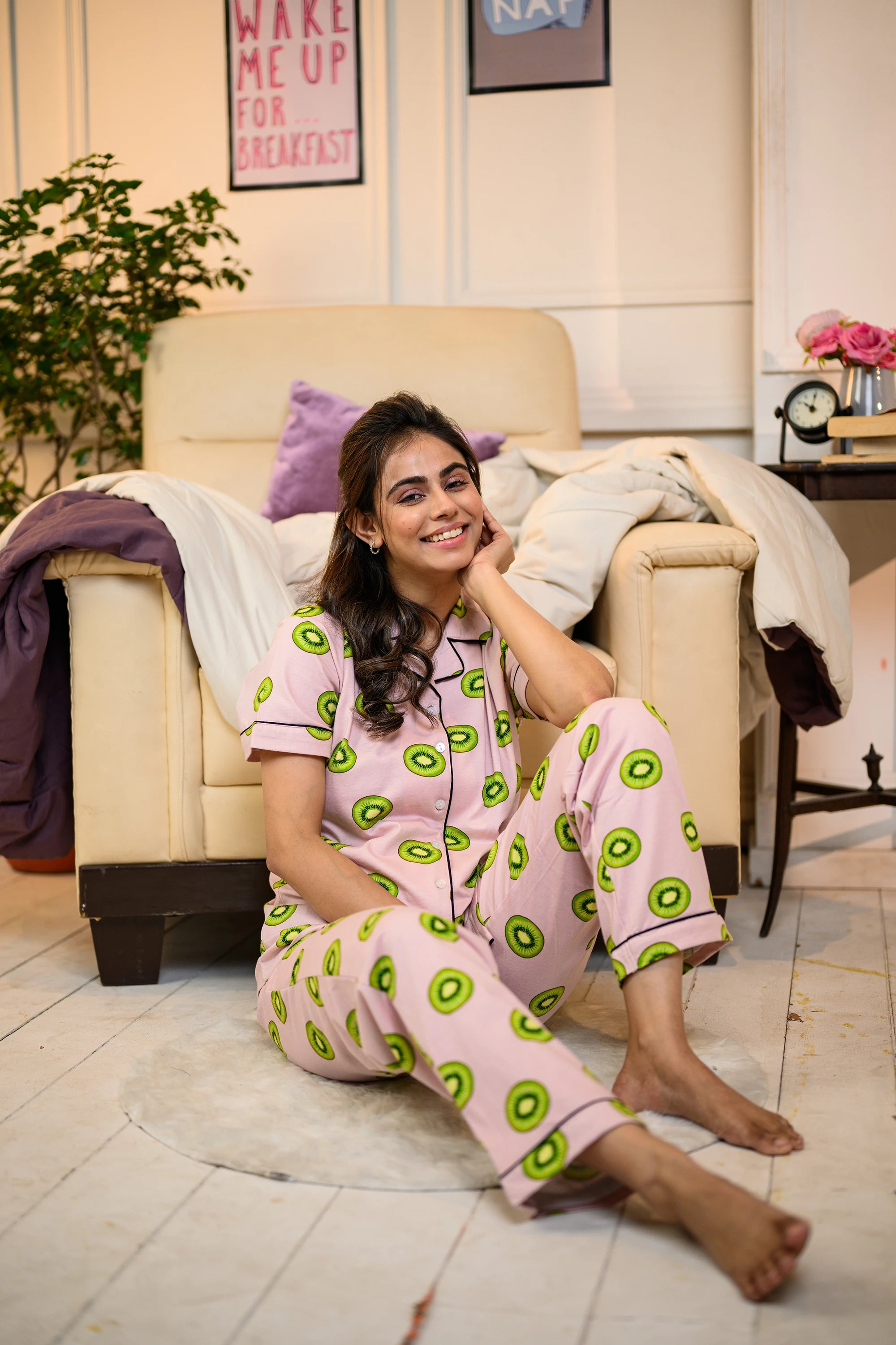 Comfortable and stylish pink Kiwi Print Pyjama Set by NapStory, worn by a woman sitting on the floor in a laid-back, homely setting.