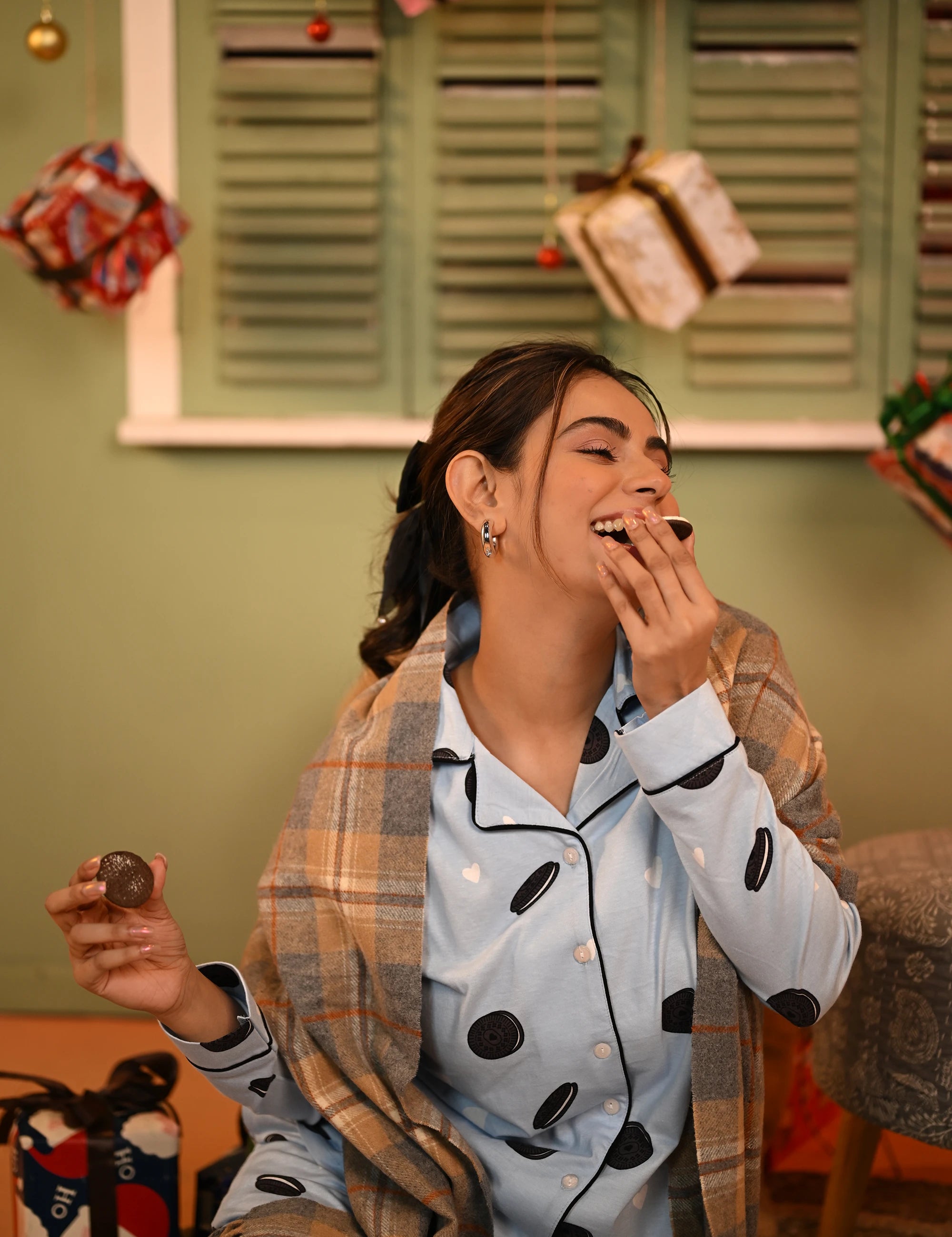 Woman smiling while holding an Oreo cookie, dressed in an Oreo print full-sleeve pyjama set.