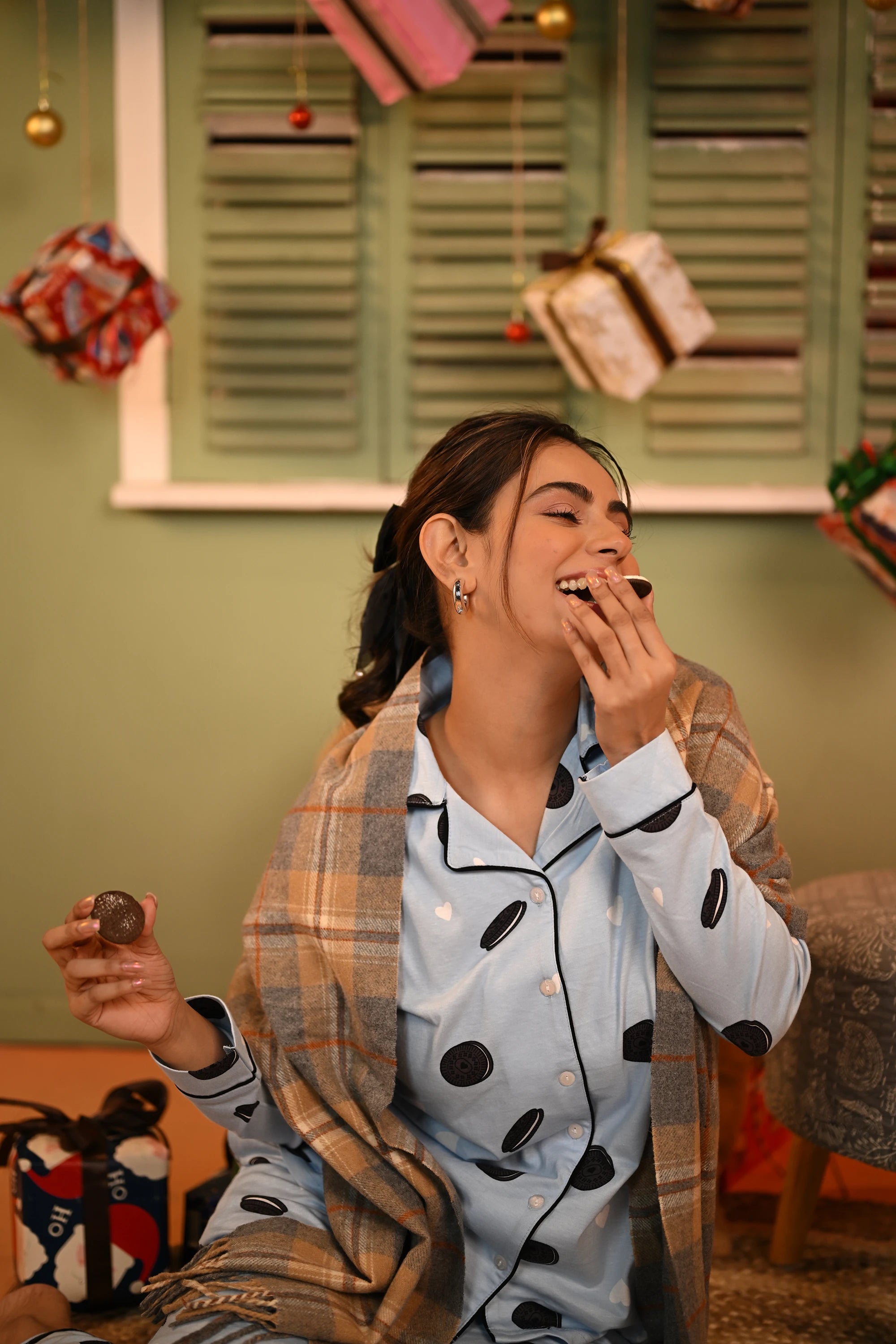 Woman smiling while holding an Oreo cookie, dressed in an Oreo print full-sleeve pyjama set.