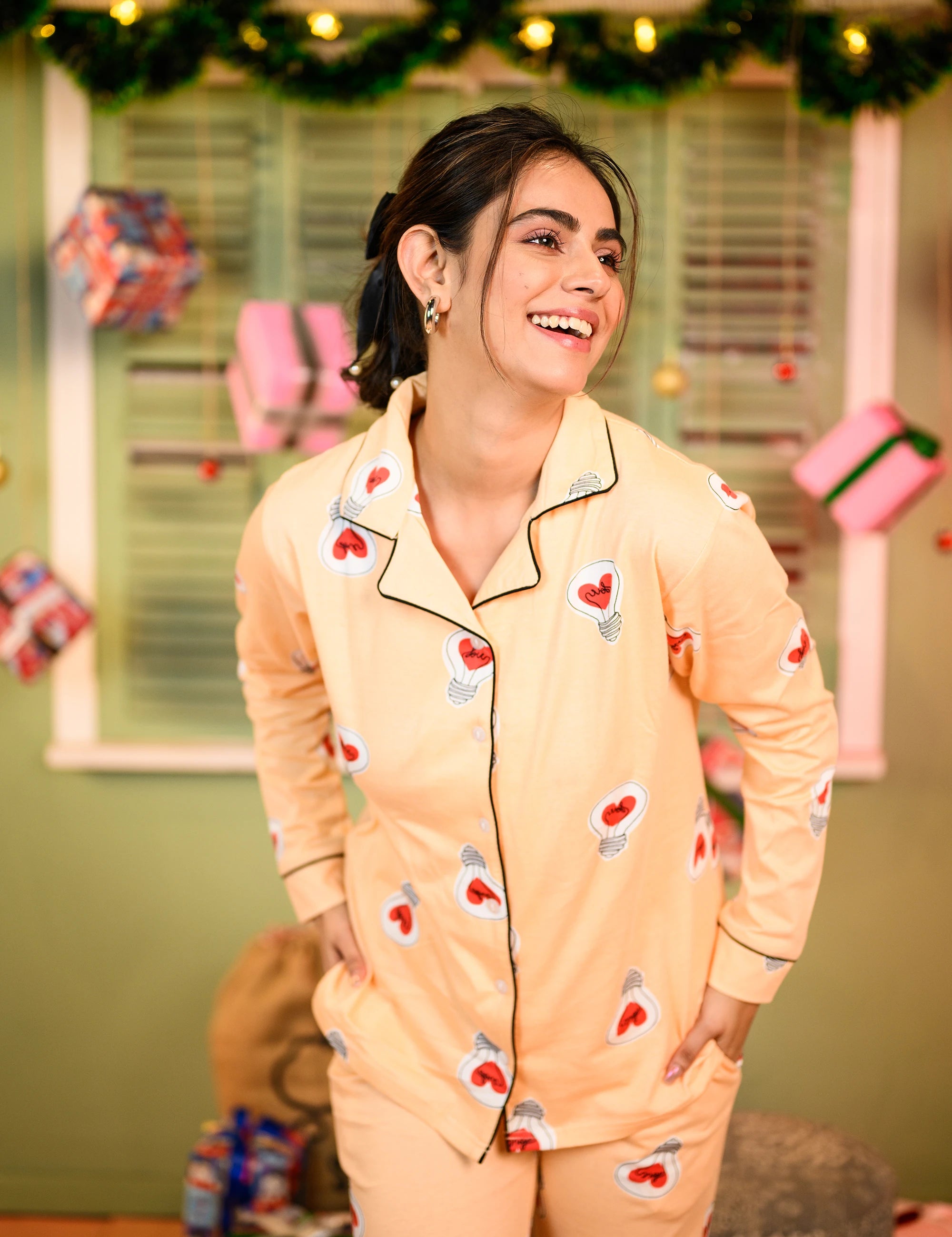 A close-up of a woman wearing a yellow full-sleeved pyjama set with a love bulb print, slightly leaning forward and smiling.