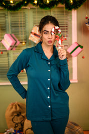 A woman smiling and playfully holding a candy cane while wearing a Teal Blue Full Sleeve Nightsuit Set, featuring a button-up top and matching pyjama pants. Cozy and stylish nightwear for women by NapStory.