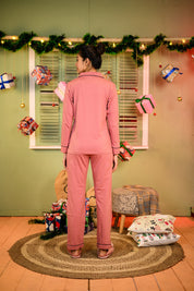 Woman wearing a ruddy pink full sleeve nightsuit set, standing with her back to the camera, looking content in a cozy pose.