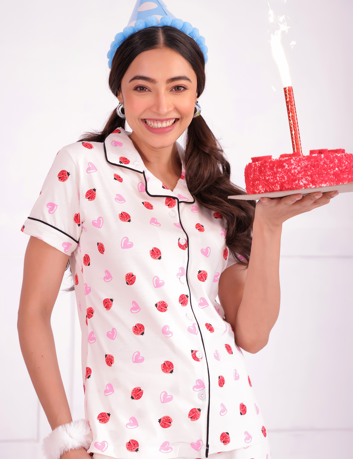 A cheerful young woman is holding a cake in her hands and wearing  Lovebug print nightwear pyjama set by NapStory