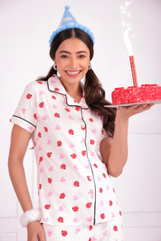 A cheerful young woman is holding a cake in her hands and wearing  Lovebug print nightwear pyjama set by NapStory