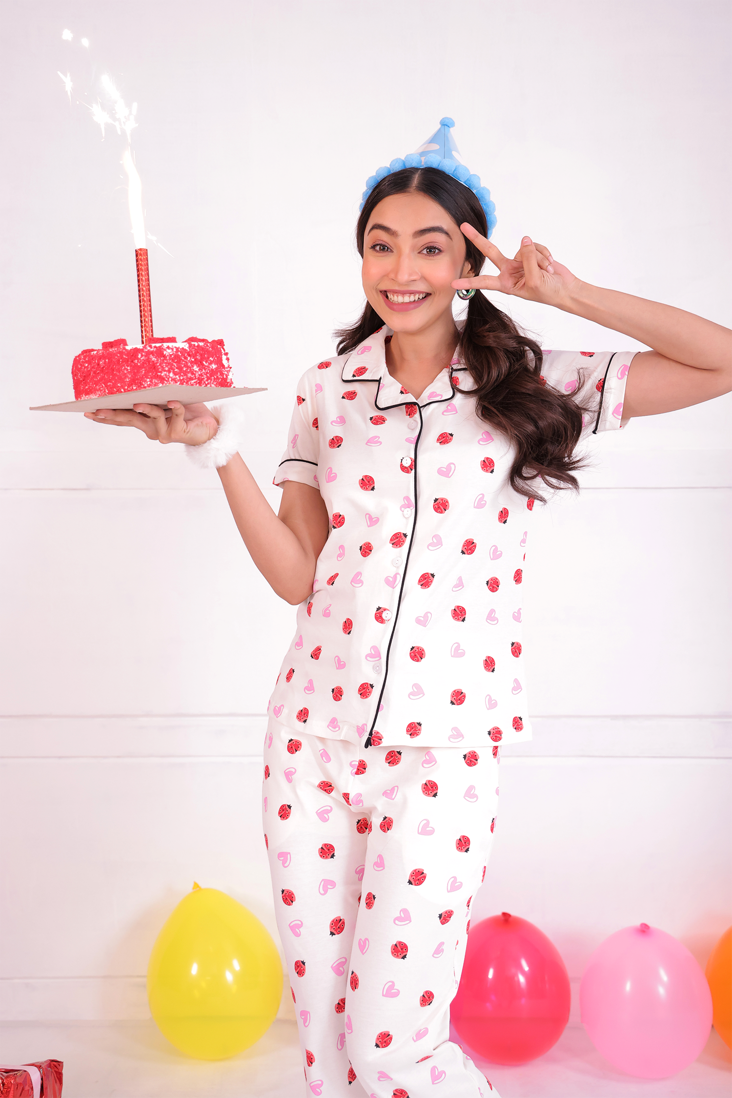 A girl wearing a Lovebug print nightwear pyjama set by NapStory and holding a cake.